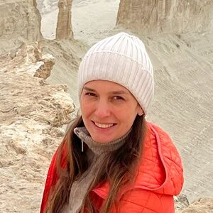 A woman in red jacket sits on a rocky peak overlooking the expansive, arid Bozzhyra landscape